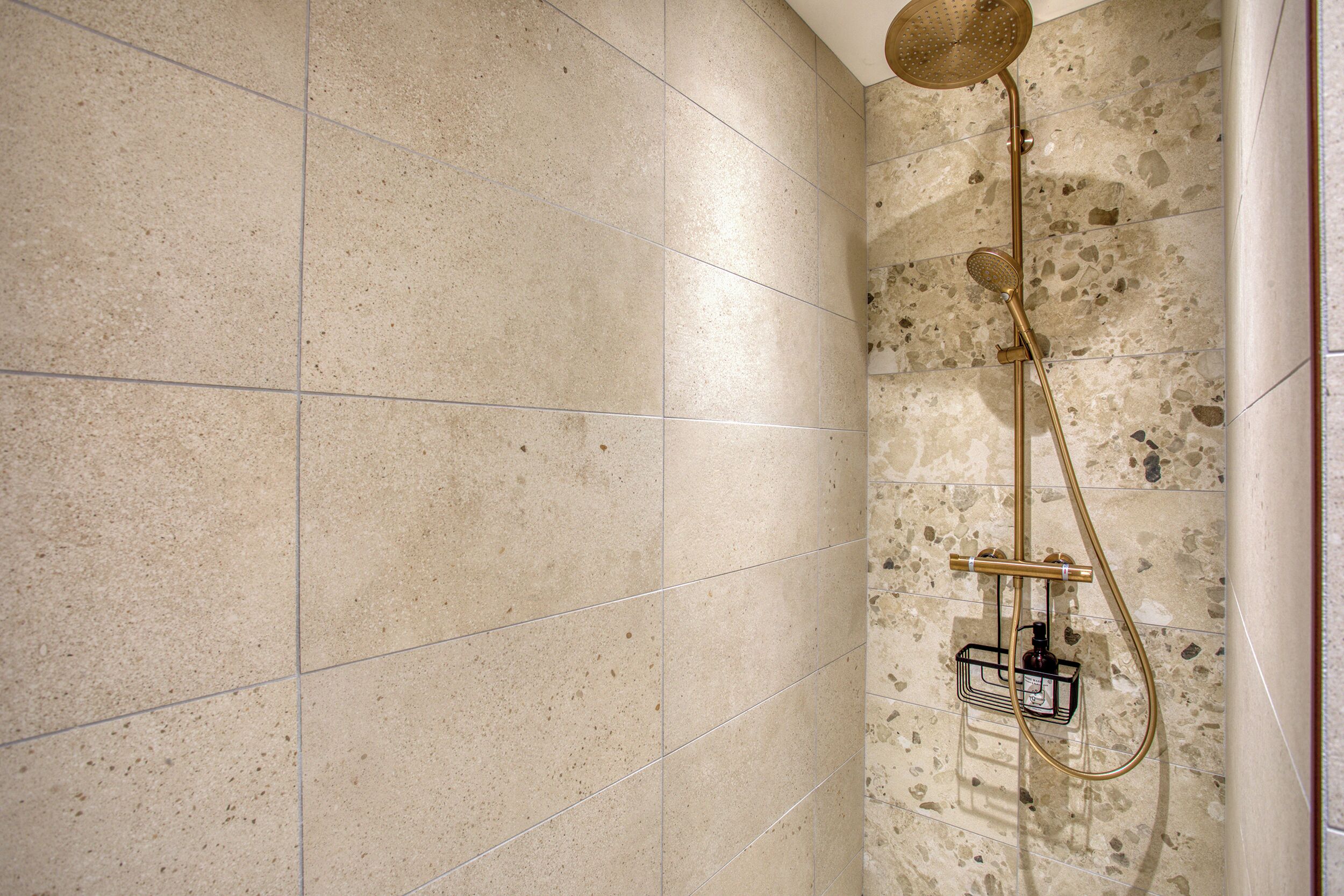 Une salle de bain avec de grandes carreaux à motifs, une pomme de douche dorée et un pommeau de douche amovible.