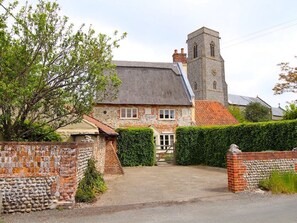 A traditional stone building with a tower, a gated entrance, and a paved driveway. - Thatch Cottage, Trunch (North Walsham)
