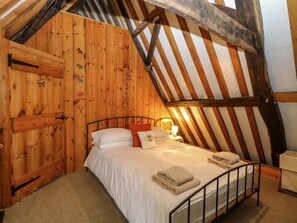 A cozy attic bedroom with a wooden sloped ceiling, a metal bed frame, and a small bedside table with a lamp. - Thatch Cottage, Trunch (North Walsham)