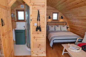 Interior de una cabaña de madera con baño, una cama y una mesita.