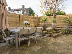 Un patio con una mesa y sillas, rodeado por una valla de madera y plantas en macetas.