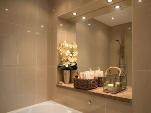 Un baño moderno con un espejo grande, una bañera y un estante con artículos de aseo y un florero con flores.