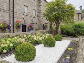 A stone building with a garden in front, including hedges and flower beds.