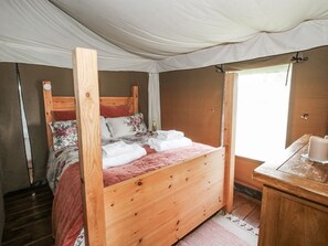 Ein hölzernes Bett mit Kopfteil, ein Nachttisch und ein Fenster mit Vorhängen.