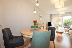 A modern living room with a round dining table, two chairs, a TV, and a view of the outside. - 17 Ocean Heights is in Newquay (Newquay)