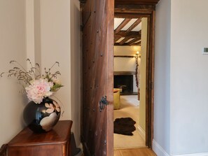 A wooden door leading to a room with a fireplace, a vase with flowers, and a fur rug on the floor. - The Old Manor House, Lifton (Lifton)
