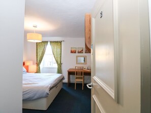 Ein Hotelzimmer mit Bett, Schreibtisch, Stuhl und einer Tür mit Griff.