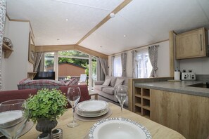 A dining area with a table set for two, a television, a sofa, and a kitchen area. - 18 Deer Glade, Landford (Salisbury)