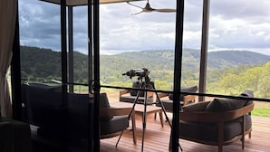 Habitación con un gran ventanal corredero que da a una terraza exterior, con una cámara sobre trípode, un sofá y dos sillones.