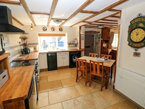 A kitchen with wooden beams, a dining table with chairs, a clock, and a window. - 1 Mill Farm Cottages, Narberth (Narberth)