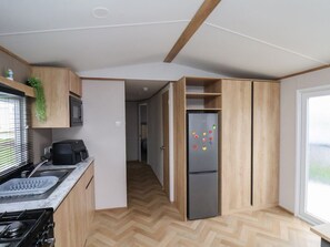 Eine kleine Küche mit Mikrowelle, Herd und Kühlschrank, Holzschränken und einem Fischgrätenparkettboden.