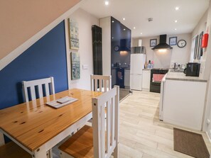 A modern kitchen with white appliances, a wooden dining table, and a blue accent wall. - The Corner House, Londonderry, Northern Ireland (Londonderry)