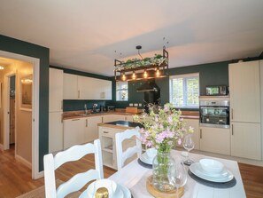 A modern kitchen with white cabinets, a dining table set with plates, glasses, and a vase of flowers. - 7 Yarnfield Parkway, Stone (Stone)