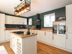 A kitchen with white cabinets, a central island, a stove, and a microwave. - 7 Yarnfield Parkway, Stone (Stone)