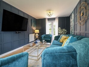 A modern living room with a large flat-screen TV, a sofa, a chair, a coffee table, and a decorative wall piece. - 7 Yarnfield Parkway, Stone (Stone)