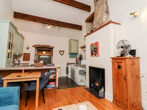 Ein gemütliches Wohnzimmer mit Kamin, Holzbalken, einem Esstisch und einer Küchenzeile.