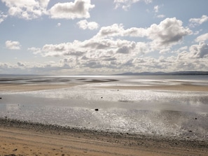A beach with a wide expanse of wet sand and gentle waves, under a partly cloudy sky.