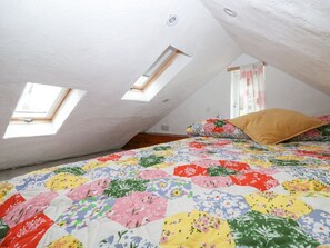 Ein Schlafzimmer im Dachgeschoss mit Dachfenstern, einer Blumen-Quiltdecke und einem Fenster mit Vorhängen.