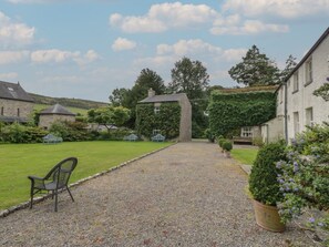 A gravel pathway leading to a building with a stone facade, surrounded by greenery and a bench. - Huntsman's Cottage, Cartmel (Grange-Over-Sands)