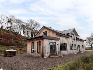 Une maison moderne en bois, dotée d’un grand garage, d’un espace extérieur couvert et d’une allée en gravier.