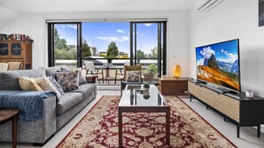 A living room with a sofa, coffee table, TV, and a view through large windows. - Comfortable 2 Bed Stay with Parking (Footscray)
