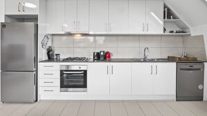 A modern kitchen with white cabinets, stainless steel appliances, and a built-in oven. - Comfortable 2 Bed Stay with Parking (Footscray)