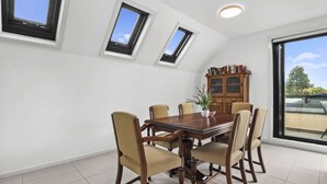A dining room with a wooden table and chairs, a bookshelf, and skylights. - Comfortable 2 Bed Stay with Parking (Footscray)
