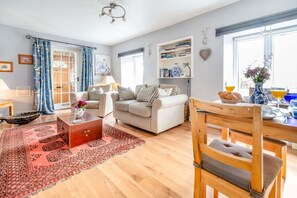 A living room with a sofa, a wooden dining table with chairs, a red trunk, and a patterned rug. - Cabbage Hall Cottage, Wetherby (Wetherby)