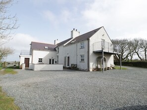 A large, single-story house with a gravel driveway and a fenced yard. - Bodegri Cottage, Church Bay (Holyhead)
