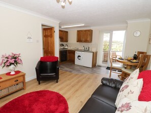 A compact living space with a kitchenette, a dining area, and a seating area with a red rug. - Bodegri Cottage, Church Bay (Holyhead)