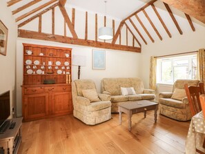A living room with wooden beams, a sofa set, a cabinet with dishes, and a window with curtains. - Byre Cottage 3 (2 bed), Storrington (Pulborough)