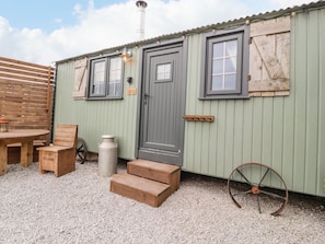 A rustic building with a door, windows, a wooden bench, a wheelbarrow, and steps leading to the entrance. - Bracken Hut at Copy House Hideaway, Earby (Barnoldswick)