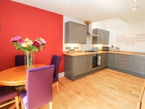 Een moderne keuken met grijze kastjes, een houten aanrechtblad en een eethoek met een tafel en paarse stoelen.