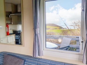 A room with a window, a view of the outdoors, a kitchen area, and a seating area.