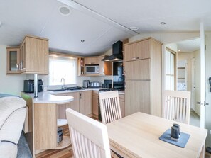 Eine kompakte Küchenzeile für Wohnmobile mit Holzausbau, einer Mikrowelle, einem Herd und einer Essecke mit Tisch und Stühlen.