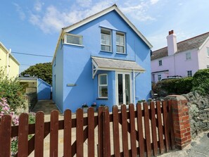 A two-story house with a blue exterior, a front porch, and a wooden fence. - Trwst Y Don, Rhosneigr (Rhosneigr)