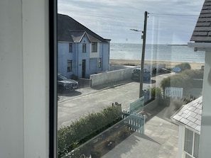 A coastal view with a building, parked cars, and a clear sky. - Trwst Y Don, Rhosneigr (Rhosneigr)