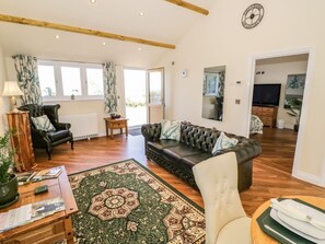 Una sala de estar con un sofá de cuero, una mesa de centro de madera, una alfombra estampada, un sillón de cuero negro y un televisor.