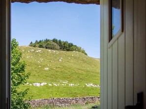 A view through a doorway of a grassy hill with a stone wall and trees. - The Barn at Amelia's Kitchen Retreat (Skipton)