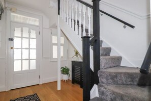 Un escalier avec des balustrades blanches, une main courante noire et un palier recouvert d’une moquette grise.