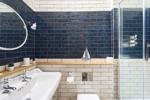 Un baño moderno con lavamanos doble, un espejo grande, una decoración náutica y una zona de ducha con mampara de vidrio.
