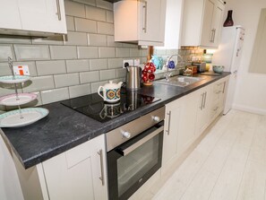 A kitchen with a black countertop, white cabinets, a stainless steel kettle, a coffee pot, and a sink. - May's Cottage, Bushmills, County Antrim (Bushmills)
