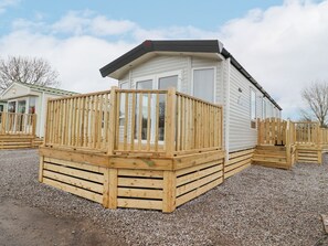 A single-story mobile home with a wooden deck, a black roof, and a gravel ground. - Giorgio, Warton in Lancashire. (Preston)
