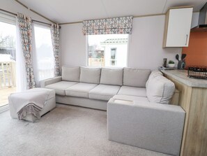A living room with a sofa, ottoman, and a window with curtains. - Giorgio, Warton in Lancashire. (Preston)
