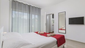 Hotellihuone, jossa on sänky, televisio, peili ja ikkuna, jossa on verhot.