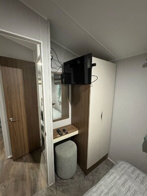 Une chambre comprenant une armoire, un lit, un petit tabouret et un téléviseur fixé au mur.