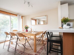 A dining area with a wooden table, chairs, a mirror, and a kitchen counter with a microwave. - Dartmoor Valley Lodge, Gunnislake (Callington)