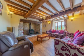 A cozy living room with a stone fireplace, wooden beams, a leather sofa, and a patterned couch. - Charming Maesgwyn Retreat in Beguildy (Knighton)