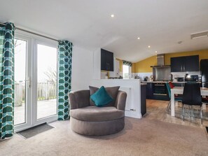 A living room with a grey sofa, a dining area with a table and chairs, a kitchen with cabinets and appliances, and a sliding glass door leading to an outdoor area.