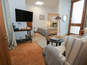 Habitació amb llit, televisió, prestatge de fusta, sofà, taula petita i terra de maó.